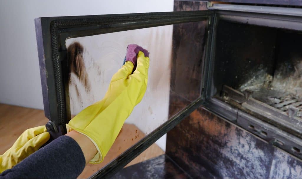 Gloved woman cleaning soot off of a fireplace with a dry sponge